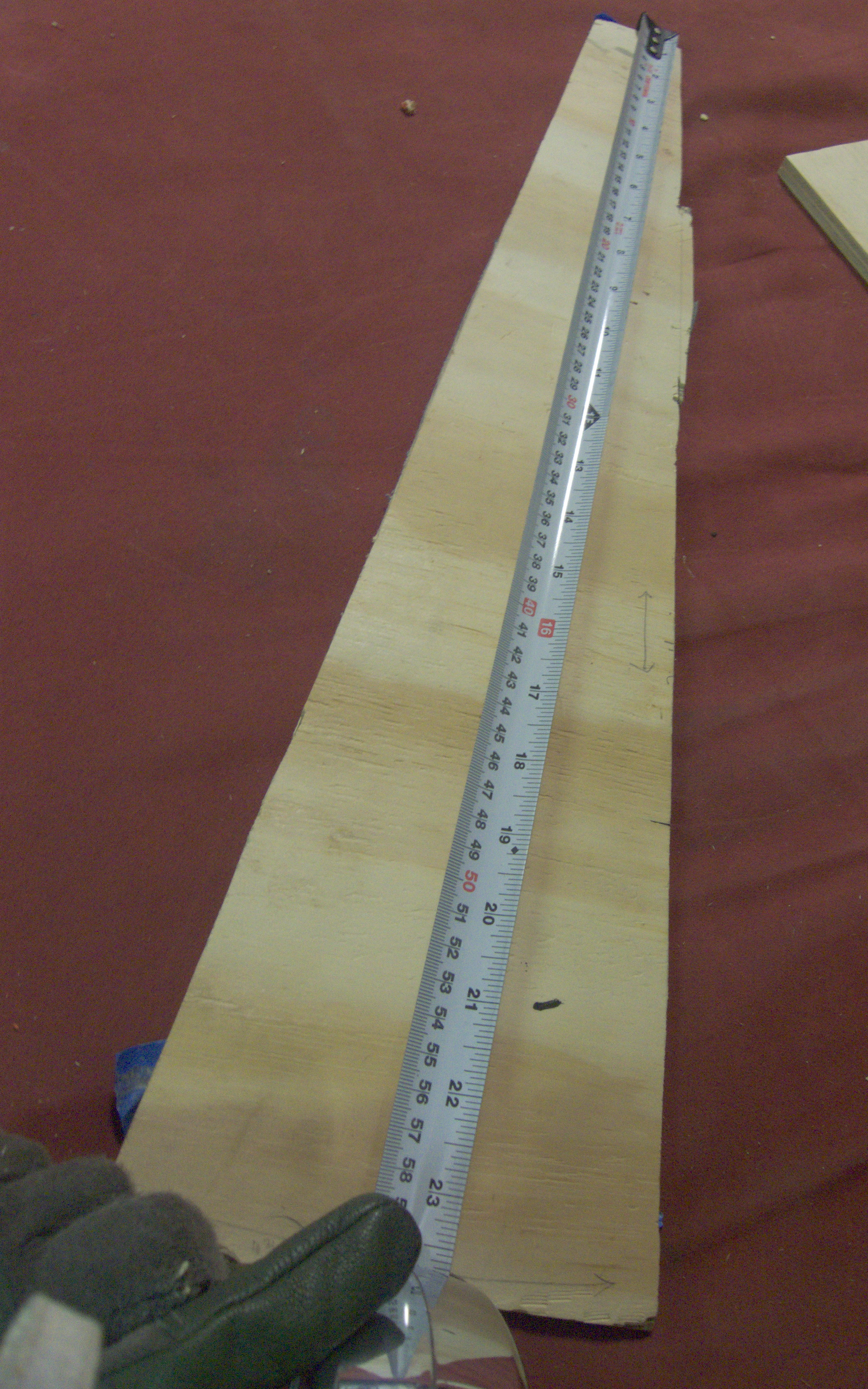a rough trapezoid, hewn from wood, with a measuring tape held against it reading a length around 23 inches / 59 cm.